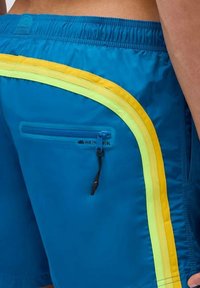 Pantaloni da nuoto blu realizzati in materiale leggero, dotati di una tasca con zip e strisce di accento giallo e verde brillanti sui lati.