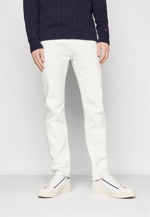 Pantaloni di cotone bianchi abbinati a un maglione a coste blu navy e sneakers bianche. Il maglione presenta un motivo testurizzato e una vestibilità aderente.