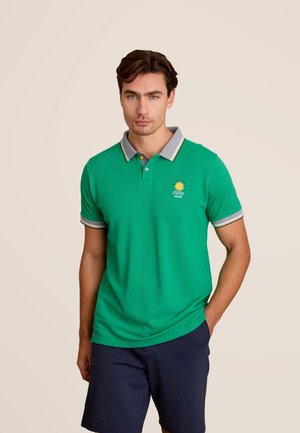Polo vert avec col et accents de manches gris, arborant un logo de soleil jaune sur la poitrine. Assorti à un short bleu marine.