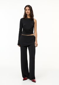 Ensemble noir en deux pièces comprenant un haut asymétrique à manches longues avec des détails froncés et un pantalon à jambes larges. Tissu texturé et doux avec une coupe ajustée.