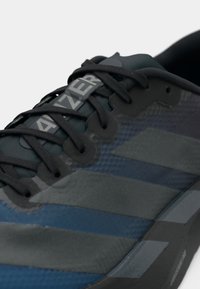 Scarpa da ginnastica blu e grigia realizzata in mesh e materiali sintetici, con lacci neri, strisce distintive e dettagli di superficie testurizzati.