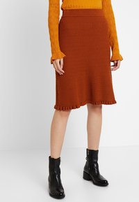 Rostfärgad ribbad stickad kjol med utsvängd nederkant och volangdetaljer, tillsammans med svarta ankelstövlar med dragkedja.