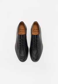 Black leather shoes with a smooth texture, rounded toe, and six eyelets for laces. Insole features printed brand name. Sole is flat.