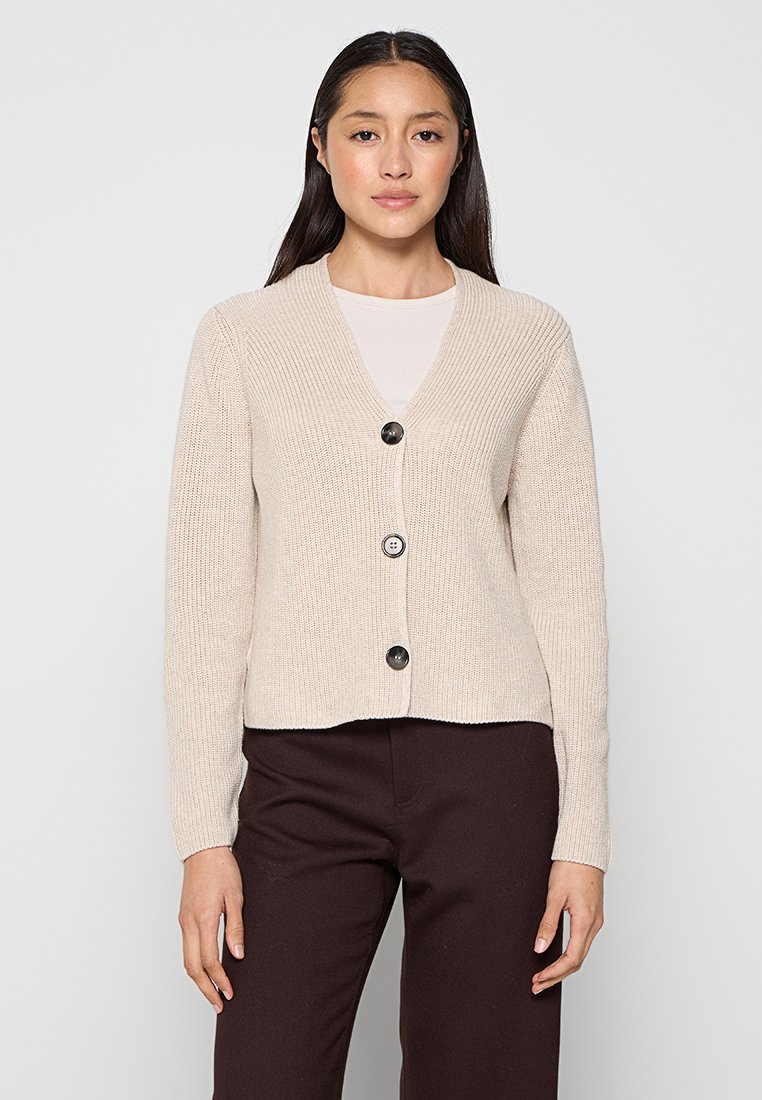 Hellbeige Strickjacke mit V-Ausschnitt, langen Ärmeln und drei dunklen Knöpfen. Der Stoff hat eine gerippte Textur und ein cropped Design.