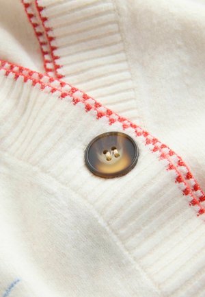 White wool fabric with ribbed texture and red stitching detail. Features a dark brown button with four holes. Close-up perspective.