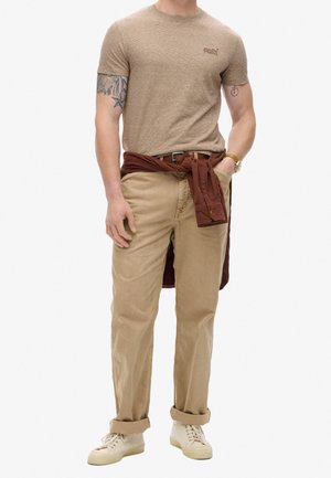 Chemise à manches courtes beige clair avec des rayures subtiles ; pantalon beige léger, poignets retroussés ; chemise bordeaux nouée à la taille ; baskets crème.