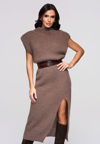 Robe tricotée marron à manches courtes, col montant et fente latérale. Complétée par une large ceinture marron autour de la taille. Texture douce.