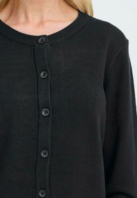 Cardigan nero realizzato in morbido materiale a maglia con scollatura rotonda, dotato di chiusura a bottoni sul davanti con bottoni neri.