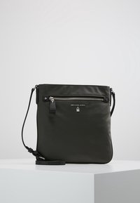 Mørkegrøn læder skuldertaske med justerbar rem, lynlåslomme foran og sølvfarvet hardware med brandlogo. Glat tekstur.