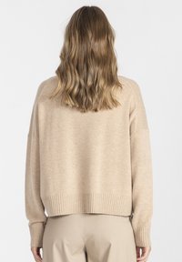 Beżowy sweter dzianinowy o luźnym kroju, z prążkowanym dołem i mankietami. Charakteryzuje się miękką teksturą i opadającymi ramionami. Wyświetlony widok z tyłu.