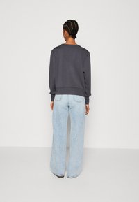 Grijze sweatshirt met geribbelde manchetten, gecombineerd met lichtblauwe wijde jeans. De outfit heeft een relaxte pasvorm en minimale details.