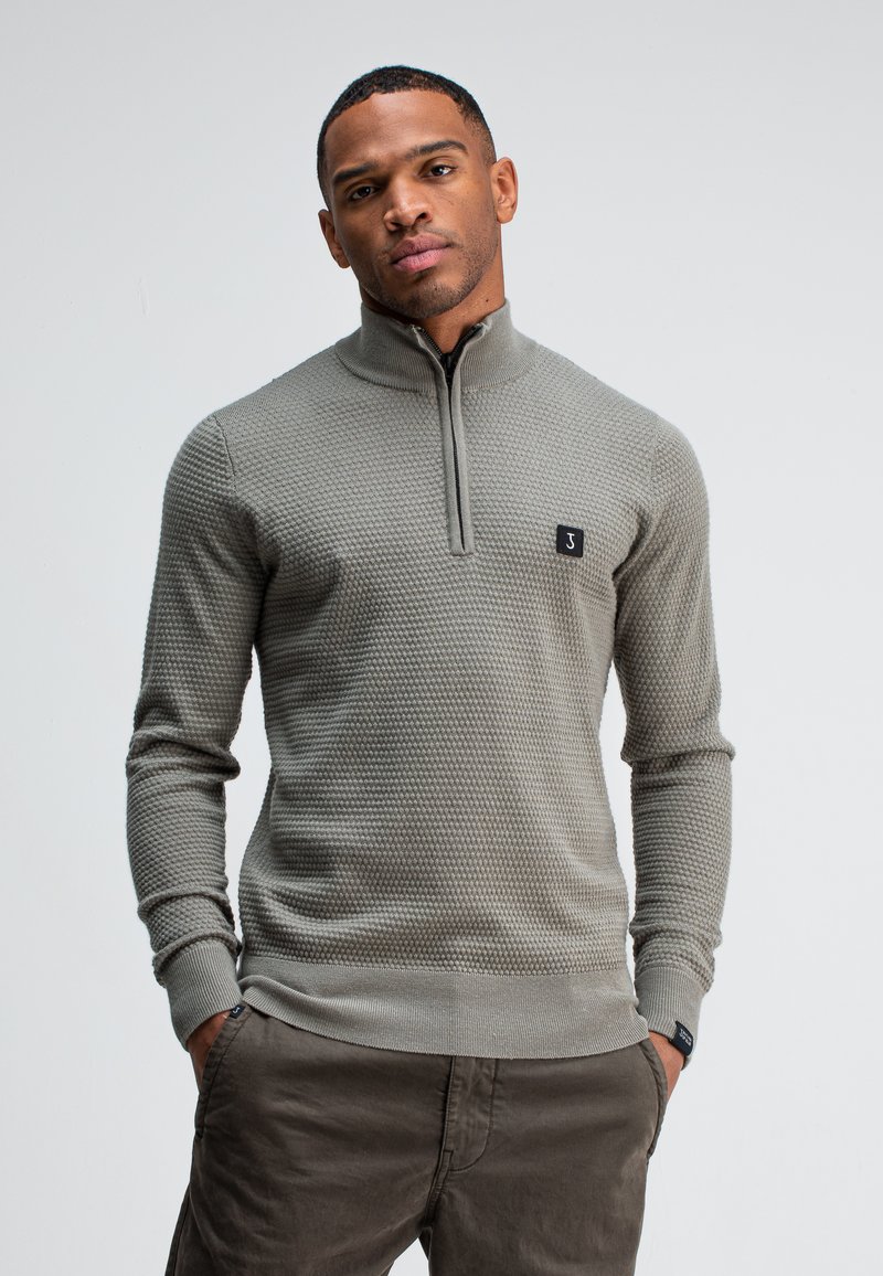 Grijze gebreide trui met een halve ritssluiting, textuurpatroon, geribde manchetten en zoom, en een klein zwart logo-opdruk op de borst.