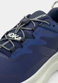 Baskets de sport bleu marine avec tige en mesh, embout renforcé, lacets élastiques et semelle blanche. Les accents comprennent le logo et le marquage GORE-TEX.