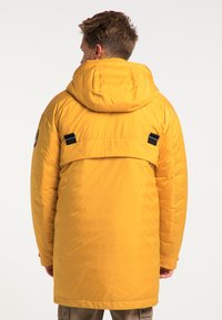 Parka izolată galbenă cu glugă, având o textură netedă, curele ajustabile la spate și un patch cu logo pe mânecă.