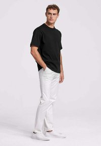 Zwarte T-shirt met korte mouwen, relaxte pasvorm, gecombineerd met smalle witte broek en witte sneakers. De stof lijkt zacht met een gladde textuur.