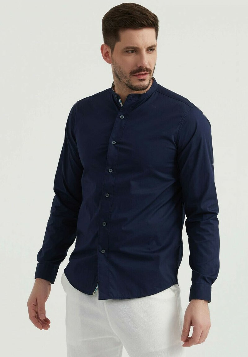 Chemise à manches longues bleu marine avec col montant, fermeture à boutons sur le devant et texture lisse ; elle s'ajuste près du corps avec une coupe ajustée.