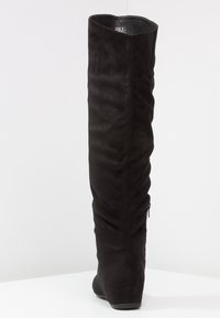 Botas negras por encima de la rodilla hechas de ante texturizado, con un diseño ajustado, un leve tacón y cremallera trasera para facilitar su uso.