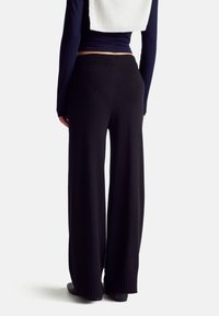 Černé široké kalhoty z měkké, texturované látky, s vysokým pasem a žebrovanými detaily na lemu.