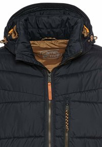 Marineblaue gepolsterte Jacke mit hohem Kragen und orangefarbenem Innenfutter. Verfügt über Reißverschluss-Schlüsse, darunter einen Hauptreißverschluss vorne und Reißverschlüsse an den Seitentaschen.