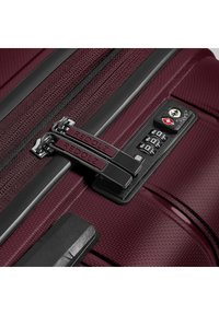 Bordeaux koffer met gestructureerd oppervlak, dubbele ritsen gelabeld "REDOLZ," en een combinatie-slot met een sleutelgat en een beveiligingsembleem.