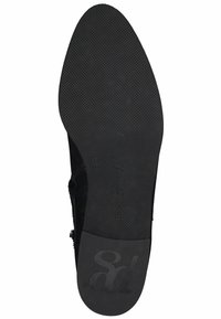 Suela de zapato negra con una superficie de goma texturizada y un logo en relieve. El zapato presenta una parte superior lisa, que destaca un diseño sencillo.