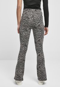 Leggings grigi con taglio a campana e motivo a strisce zebra nere. Il tessuto sembra elastico, con una texture liscia e una vita alta.