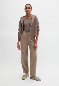 Gebreide beige capuchontrui met een geribbelde textuur, gecombineerd met beige broek met hoge taille en lichtbeige instapschoenen. Soepele, ontspannen pasvorm.