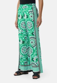 Grüne gemusterte weite Hosen mit Blumen- und geometrischen Designs, einem flachen Bund und kontrastierenden schwarzen Akzenten an den Seiten.