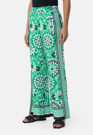 Groene broek met een wijd model, versierd met bloemen- en geometrische patronen, een platte tailleband en contrasterende zwarte accenten langs de zijkanten.