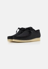 Scarpe nere in mesh con punta rotonda, caratterizzate da un design con lacci e suole in gomma beige a contrasto. Parte superiore testurizzata con cuciture visibili.