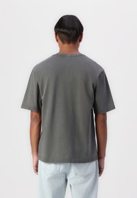 Dark gray cotton T-shirt with short sleeves, crew neck, and straight cut, worn with light blue jeans. No distinct patterns or accents.