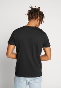 Camiseta negra de manga corta con cuello redondo clásico, tejido de algodón, suave al tacto y sin logotipos ni patrones visibles.