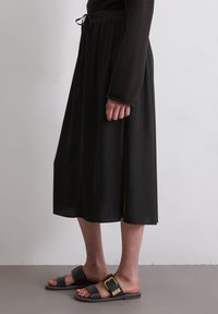 Gonna nera midi con vita regolabile, caratterizzata da una fessura laterale. Abbinata a sandali scuri con un accentuato fibbia dorata.
