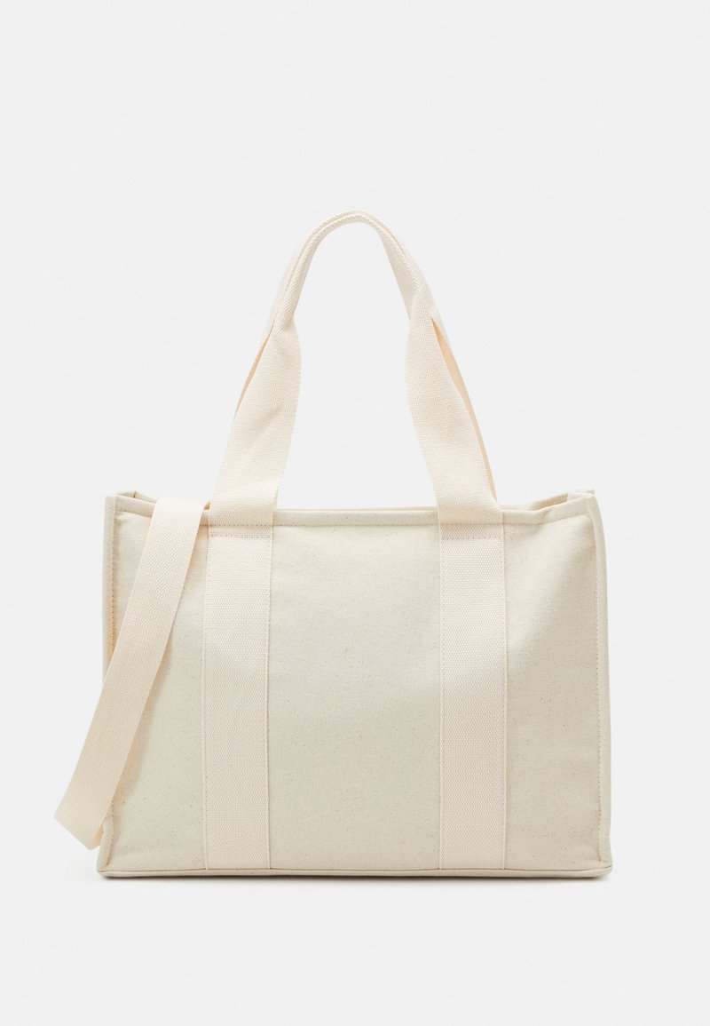 Sac fourre-tout rectangulaire en toile beige avec deux petites poignées et une longue bandoulière sur fond blanc.