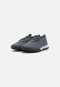 Zapatillas deportivas grises con una superficie texturizada, diseño con cordones y suela robusta. Las características notables incluyen perforaciones y un acento blanco en contraste.