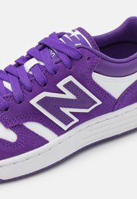 Sneaker in suede e pelle viola con dettagli e lacci bianchi. La scarpa presenta un audace logo "N" e una suola in gomma testurizzata.