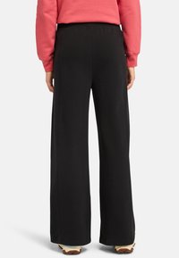 Svarta vida byxor med en avslappnad passform, tillverkade av en mjuk bomullsblandning, med resår i midjan och utan synliga mönster eller detaljer.