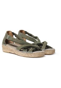 Žalios velūro espadrilės sandalo su kryžminėmis strapomis ir pintu jute viduriu. Yra šviesaus atspalvio pintas kraštas ir plokščias padas.