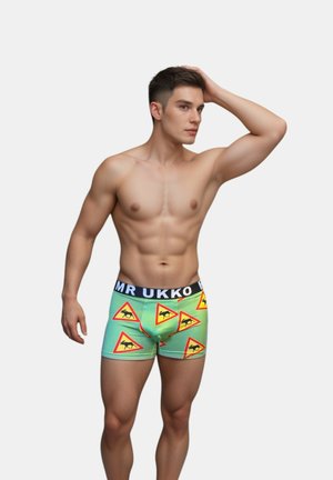 Boxer shorts verdi con motivo a triangolo di avvertimento che presenta silhouette nere, e una cintura nera con il testo "MR UKKO".