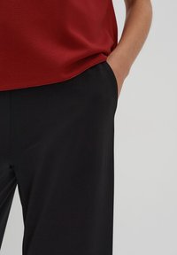Rote Bluse mit kurzen Ärmeln, kombiniert mit schwarzen weit geschnittenen Hosen. Die Hose hat Seitentaschen. Glattes Material mit matter Oberfläche.