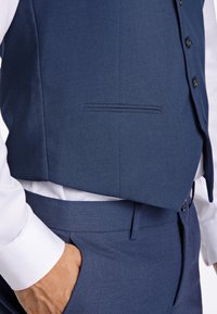 Mörkblå väst med en slät yta, försett med knäppning och en liten ficka. Komplementär vit skjorta med rund krage.