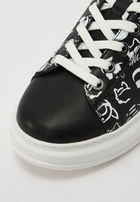 Fekete sneaker, fekete-fehér mintázatú felsőrésszel, fehér fűzőkkel és texturált fekete orr résszel, vastag fehér talpon.