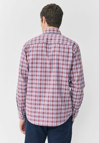 Kariertes Hemd in Rot, Weiß und Blau mit langen Ärmeln, Knopfkragen und abgerundetem Saum. Das Material wirkt strukturiert.