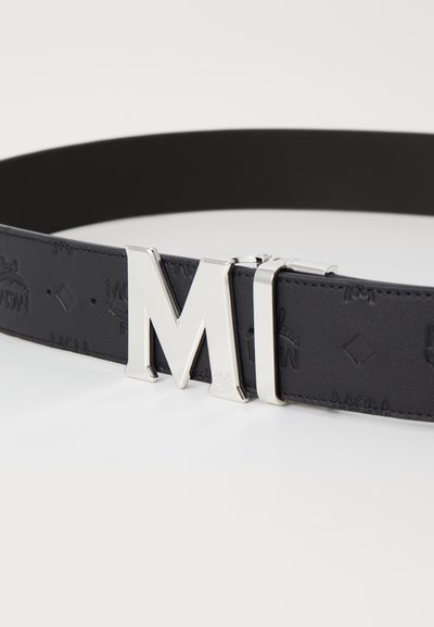 Black leather belt featuring a large silver "M" buckle. The belt is embossed with a subtle pattern and has a smooth texture.