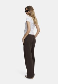 Bruna sweatpants med avslappnad passform och fickor, i kombination med en figursydd vit t-shirt. Modellen bär mörka solglasögon och har långt hår.