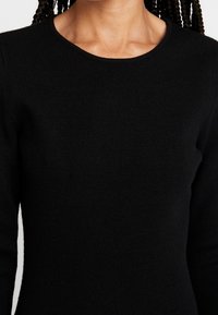 Schwarzer Strickpullover mit Rundhalsausschnitt und langen Ärmeln, der eine weiche Textur und eine taillierte Silhouette zeigt.