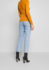 Pull ajusté jaune moutarde à rayures horizontales, associé à un jean bleu clair à jambes droites et des bottines à talons hauts noires.