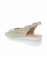 Sandal beige con design a tagli, cinturino alla caviglia regolabile e suola piatta bianca. Parte superiore testurizzata con forme geometriche.