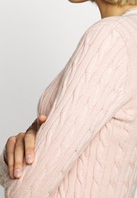 Vaaleanpunainen palmikkoneulepaita, jossa on teksturoitu kuvio ja resorireunukset hihoissa, istuva leikkaus.