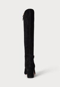 Bottes noires en daim montant jusqu'au genou avec un haut talon bloc, une fermeture éclair sur le côté et un accent de sangle cousue autour de la cheville. Texture lisse.